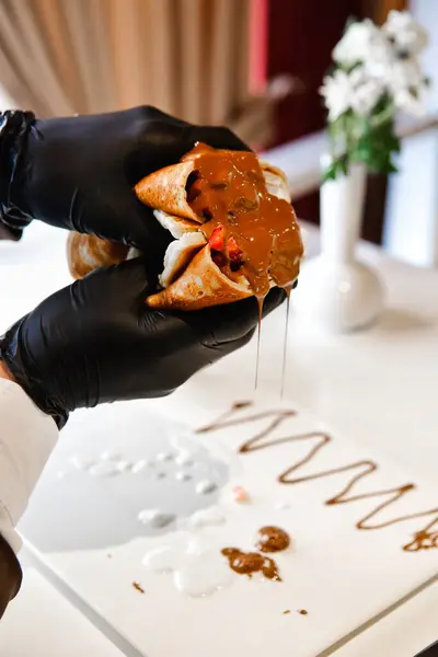 stock image Gloved hands carefully hold a crepe filled with fruit and drizzled with chocolate.