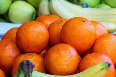 Bir yığın parlak turuncu portakal yakın çekim, arka planda biraz muz ve elma ile.