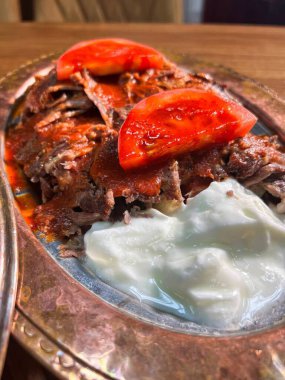 Geleneksel Türk donör kebabının yakın çekimi yoğurt ve domatesli bakır tabakta servis ediliyor.