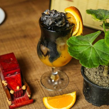 A refreshing cocktail with orange and charcoal, garnished with an orange slice and served in a stemmed glass. clipart