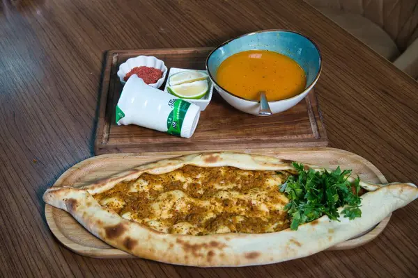 stock image A close-up shot of a delicious Turkish pide, a flatbread filled with savory ingredients, served with a bowl of soup and a side of fresh parsley.