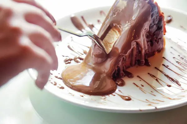 stock image A person uses a fork to cut into a slice of chocolate cake, with the rich chocolate sauce dripping onto the white plate.