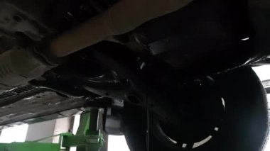 Bir araba kaldırılıyor, aracın altını gösteren bir asansör. Tamirci olası tamiratlar için arabayı inceliyor..