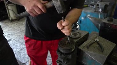 Bir tamirci, garajda dururken araba parçalarını tamir etmek için çekiç kullanır..
