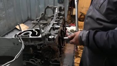 Bir tamirci, ingiliz anahtarıyla bir motor bloğunda sürgüyü sıkılaştırır. Motor parçalandı ve bir tezgahın üzerine yerleştirildi..