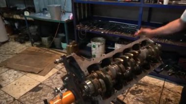 Bir tamirci dağınık bir atölyede parçalanmış bir araba motoru üzerinde çalışır..