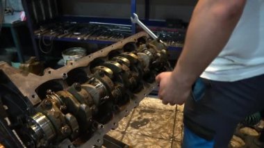 Bir tamirci garajda bir araba motoru üzerinde çalışır, sürgüyü sıkıştırmak için İngiliz anahtarı kullanır..