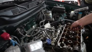 Bir tamirci bir arabanın motoru üzerinde çalışır, parçaları ayarlar ve tamir eder..