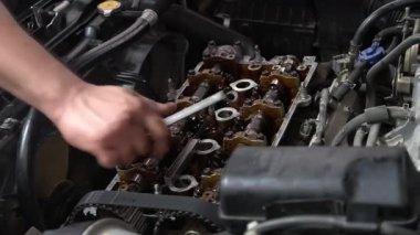 Bir tamirci sürgüyü sıkıştırmak için İngiliz anahtarı kullanarak bir arabanın motoru üzerinde çalışır. Motor açık, içsel işleyişi ortaya çıkarıyor..