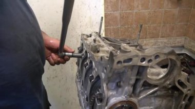 Bir tamirci, ingiliz anahtarıyla bir motor bloğunda sürgüyü sıkılaştırır. Motor bloğu kısmen parçalanmış, iç işlemleri gösteriyor.