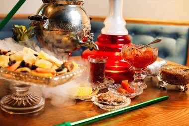 Çaydanlık, çaydanlık, bir bardak çay, bir kase meyve ve diğer tatlı ikramlarla dolu bir masa..