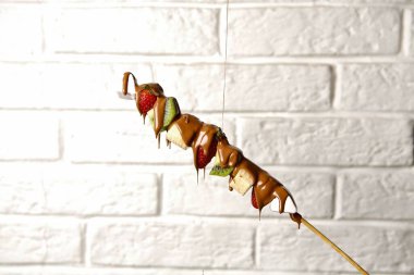 Çikolataya batırılmış bir meyve şişi, beyaz bir duvara asılı..