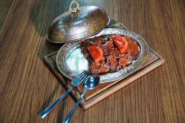 Bir tabak Türk donör kebabı, yoğurt ve domates dilimleriyle servis edilmiş, ahşap bir kesim tahtasının üzerinde dinleniyor..