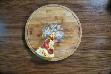 Tek dilim pizza ve malzemeler tahta kesme tahtasının üzerinde duruyor..