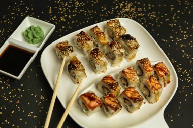 Soya sosu ve wasabi ile servis edilen sushi dürümlü beyaz tabak - somon, yılan balığı, salatalık - susam tohumlu