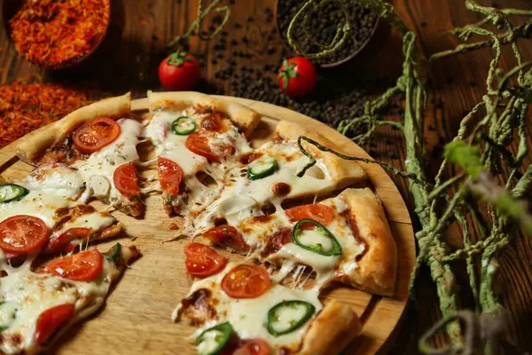 Domatesli, biberli ve ahşap kesim tahtasındaki peynir soslu bir pizza..