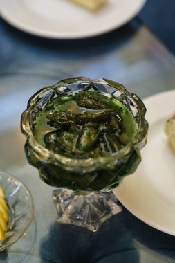 Tuzlu yeşil zeytinlerle dolu cam bir kase tabaklar ve bulanık bir arka planla çevrili bir masada oturur..