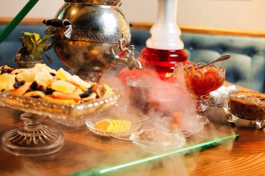 İçinde gümüş çaydanlık, çay fincanı, meyve ve nargile bulunan geleneksel Türk çay servisi olan bir masa..