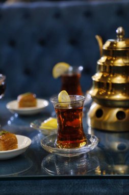 Bir bardak limon dilimli Türk çayı, bir tabak baklava ve bir çaydanlık cam tepeli bir masada oturur..