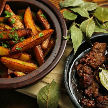 Kırsal ahşap bir masaya yakın, içinde kızarmış patates ve ağır ateşte pişmiş et bulunan iki tabak..