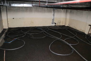 Duvarında su lekesi ve kablolar olan beton bir bodrum katı..