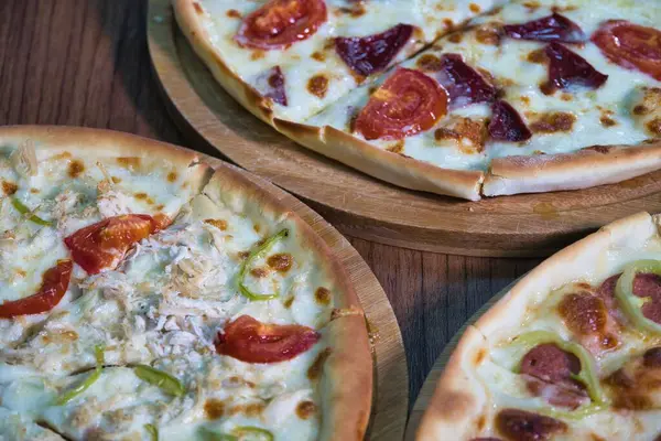 Tavuklar, biberler ve domatesler de dahil olmak üzere farklı malzemeli üç pizzanın yakın plan görüntüsü..
