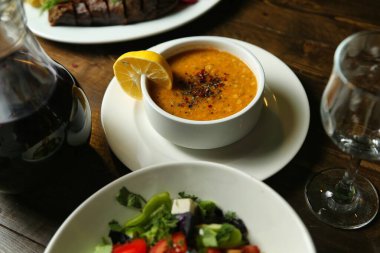 Limon ve baharatla süslenmiş bir tabak mercimek çorbası, yanında salata ile servis edilir..
