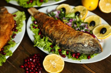 Beyaz bir tabakta, marul, limon, kırmızı soğan, zeytin ve nar tohumlarıyla servis edilen kızarmış balık..