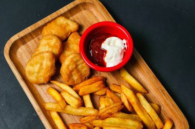 Kızarmış tavuk nugget ve patates kızartması daldırma soslu ahşap tabakta..