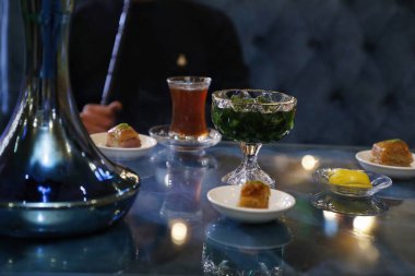 Bir bardak çay, çeşitli tatlılar ve mavi nargile tabanlı bir masa..