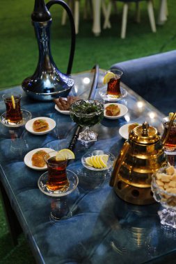 Çay, şeker ve limon dilimli bir masa, nargile ve ön planda altın çaydanlık..