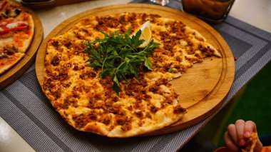 Kısmen yenmiş maydanozlu Türk pizzası ve tahta üzerinde limon dilimi..