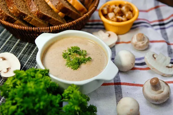 Maydanozla süslenmiş, taze ekmek ve mantarla servis edilmiş bir kase kremalı mantar çorbası..