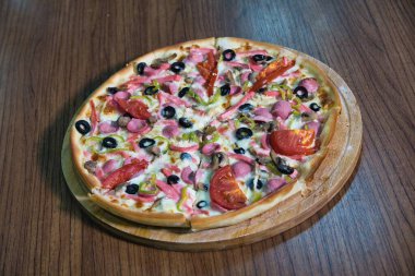 Tahta bir tahtanın üzerinde zeytin, biber ve sosis ile yakın plan bir pizza..