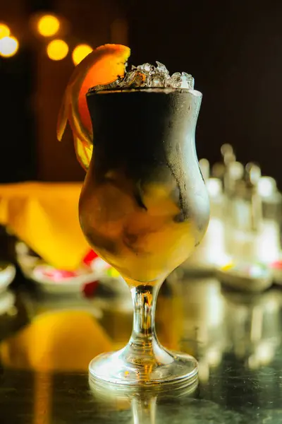 stock image A close-up of a cocktail in a glass with ice and an orange peel garnish. The drink is a dark color with a yellow layer underneath.