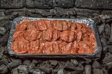 Bir tepsi çiğ köfte kızgın kömür briketlerinin üzerinde ızgaraya hazır bekliyor..