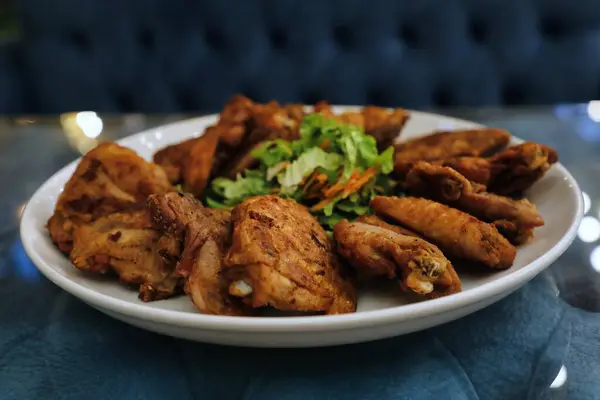 Kızarmış tavuk kanadı ve beyaz tabakta servis edilen bir salata..