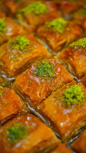 Tepside düzgünce dizilmiş fıstıklı yeni yapılmış bir baklava resmi..