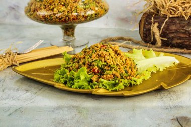 Closeup of a Turkish Bulgur salad, known as kisir, with parsley and mint. The salad is served on a gold leaf-shaped plate with lettuce garnish. clipart