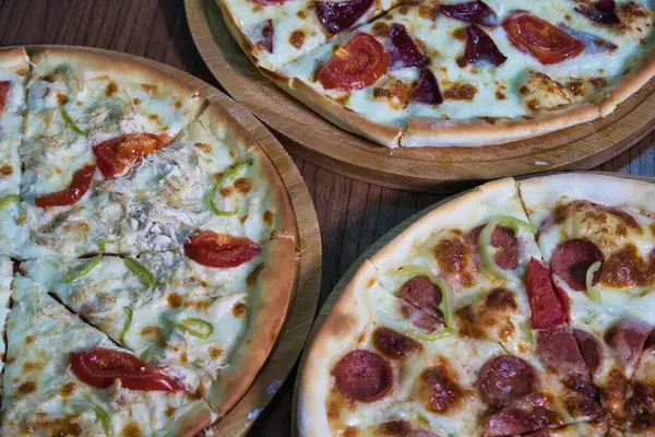Üç farklı pizza, dilimlenmiş ve yemeye hazır, ahşap tahtalarda oturuyorlar..