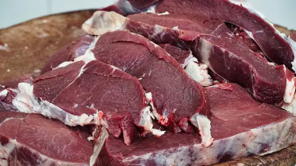 Dilimlenmiş ve pişirilmeye hazır çiğ biftekler ahşap bir kesim tahtasının üzerinde sergileniyor..