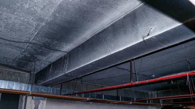 Açığa çıkmış borular ve kablolarla beton bir tavana yakın plan..