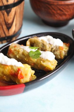 Yoğurt sosu ve maydanozla kaplı siyah ve kırmızı tabakta üç lahana rulosu..