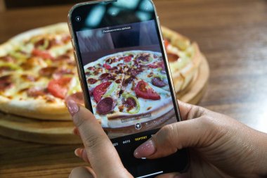 Pizzanın fotoğrafını çeken bir insan eli telefonu tutar..