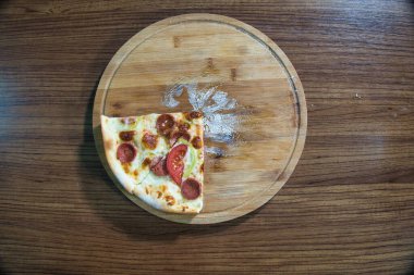 Biberli, domatesli ve peynirli bir dilim pizza ahşap bir masanın üzerinde duruyor..