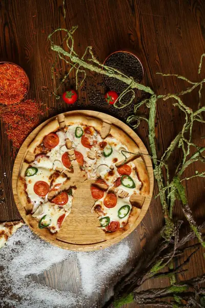 Kısmen yenmiş domates ve jalapeno soslu bir pizza ahşap bir tahtanın üzerinde oturur..