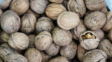 A close-up view of shelled walnuts in a container, showing their textured shells and a few open ones revealing the nut inside. clipart