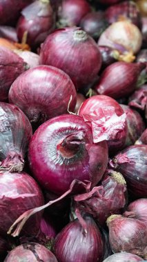 Kırmızı soğanların yakın çekimi, canlı mor derilerini ve karmaşık dokularını sergileyerek, bir market tezgahında üst üste yığılmıştı..