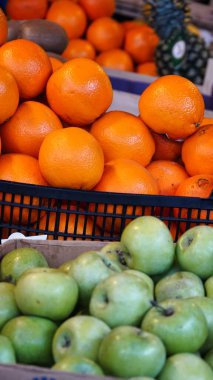 Siyah plastik bir sandıkta taze portakallar ve ahşap bir sandıkta yeşil elmalar sergilenen bir market tezgahının yakın görüntüsü..