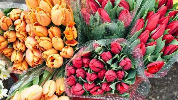 İki buket lale, biri turuncu, biri kırmızı, plastiğe sarılmış ve bir markette sergilenmiş..